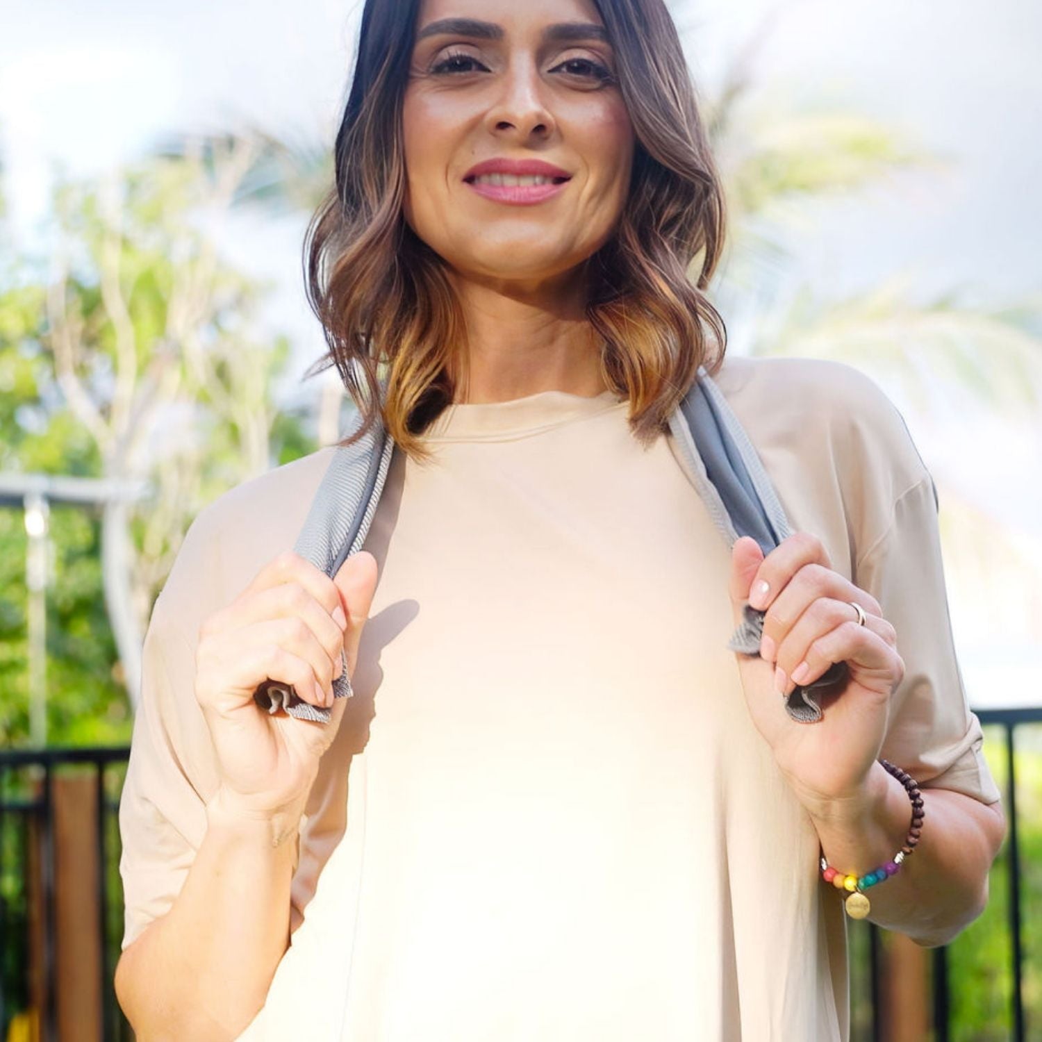 Woman holding MenoChill™ Cooling Towel while wearing beige tee, outdoors in natural light.