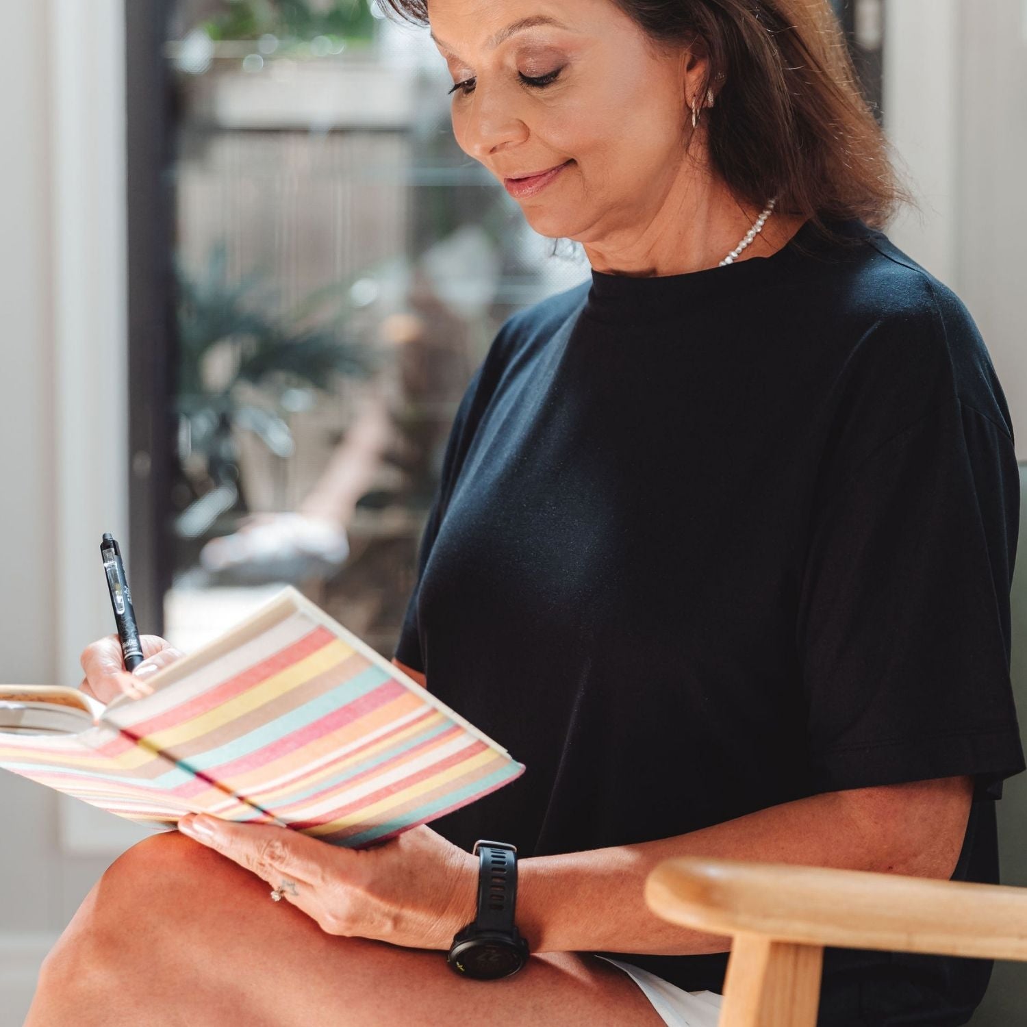Woman journaling indoors wearing Lyvora Noir Breeze Tee — calm lifestyle shot